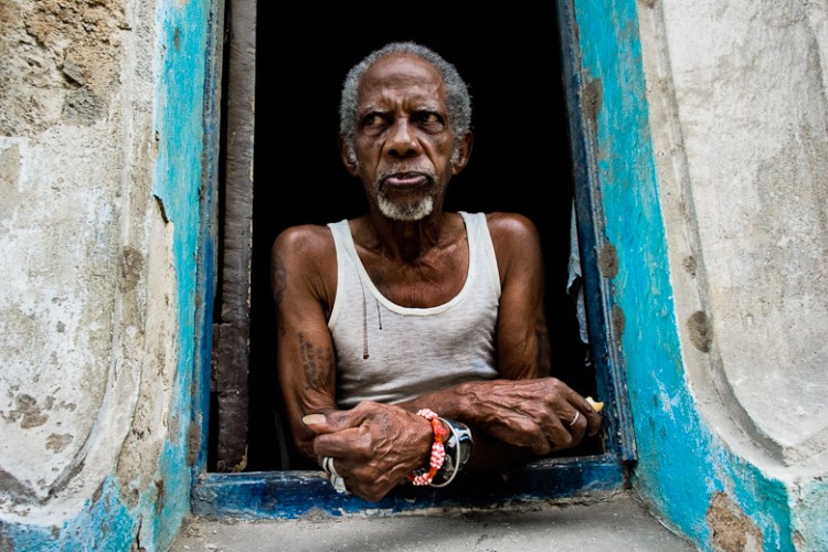 A Cuban man, the Palo Monte priest, wearing a typical red and white bracelet, looks out of the window in Havana, Cuba, August 19, 2009. The Palo religion (Las Reglas de Congo) belongs to the group of syncretic religions which developed in Cuba amongst the black slaves, originally brought from Congo during the colonial period. Palo, having its roots in spiritual concepts of the indigenous people in Africa, worships the spirits and natural powers but can often give them faces and names known from the Christian dogma. Although there have been strong religious restrictions during the decades of the Cuban Revolution, the majority of Cubans still consult their problems with practitioners of some Afro Cuban religion.