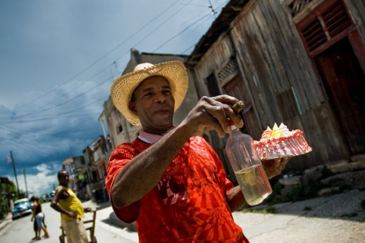 A Cuban man hurrying for a fiesta, holding a bottle of rum, smoking a cigar and carrying a sweet cake in his hand, Santiago de Cuba, Cuba, 3 August 2008. Although the overall situation in Cuba is tough and life is challenging there, Cubans never forget to celebrate, to call for a fiesta. About 50 years after the national rebellion led by Fidel Castro and adopting the communist ideology shortly after the victory, the Caribbean island of Cuba is the only country in Americas having the socialist political system. Although the Cuban state-controlled economy has never been developed enough to allow Cubans living in social conditions similar to the US or to Europe, mostly middle-age and older Cubans still support the Castro Brothers' regime and the idea of the Cuban Revolution. Since the 1990s Cuba struggles with chronic economic crisis and mainly young Cubans call for the economic changes.